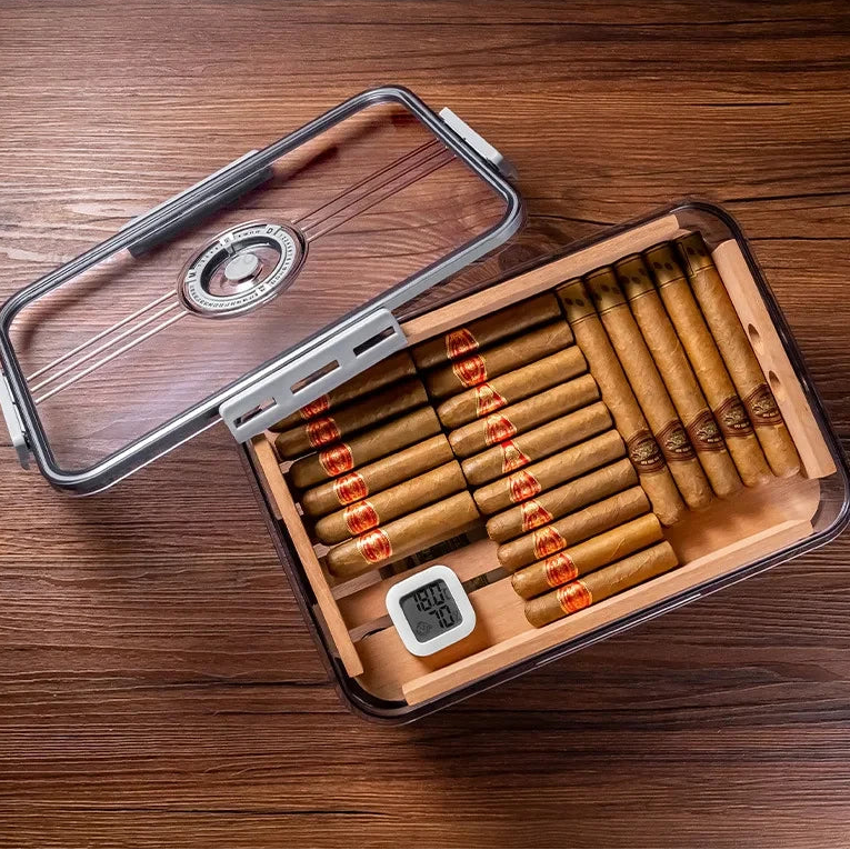 Cigar humidor with cigars and a digital thermometer on a wooden surface.